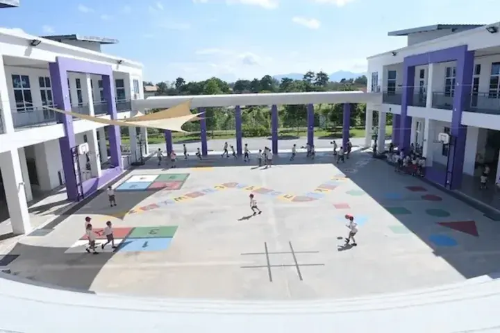 Modern school playground with colorful hopscotch and alphabet markings, surrounded by white and purple buildings under a shade sail.