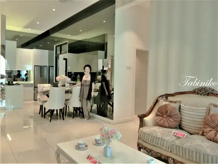 Woman standing in a modern luxury showroom with a dining area, kitchen, and classic sofa.