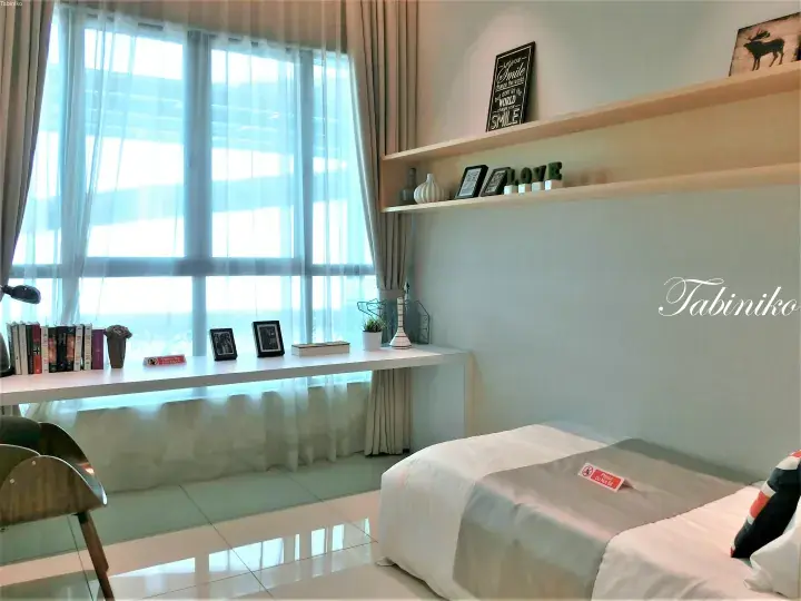 Bright hotel room with a neatly made bed, long window desk, and shelves featuring decor and a motivational quote.