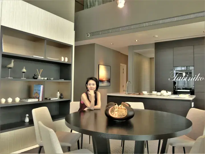 现代公寓内，一位女士坐在时尚餐桌旁，背景可见开放式置物架和厨房岛台。