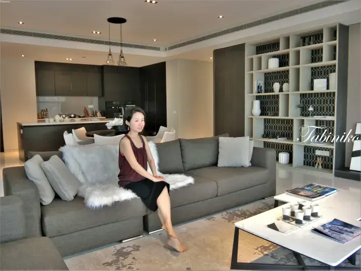 现代豪华公寓客厅中坐在灰色沙发上的女性，配有开放式厨房和内置置物架。