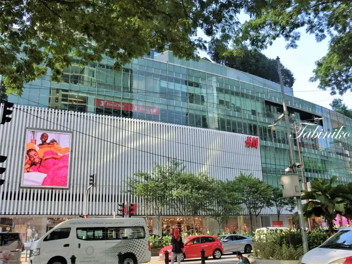 吉隆坡现代玻璃建筑，设有H&M和健身中心招牌，配有大型数字广告牌和街道交通。