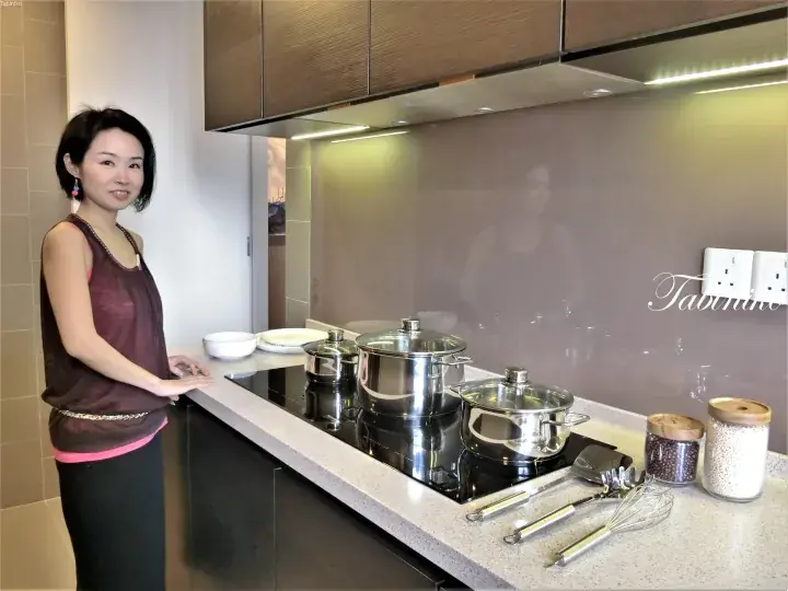 不锈钢锅具摆放在电磁炉上，大理石台面和玻璃背板的现代厨房里微笑的女性。
