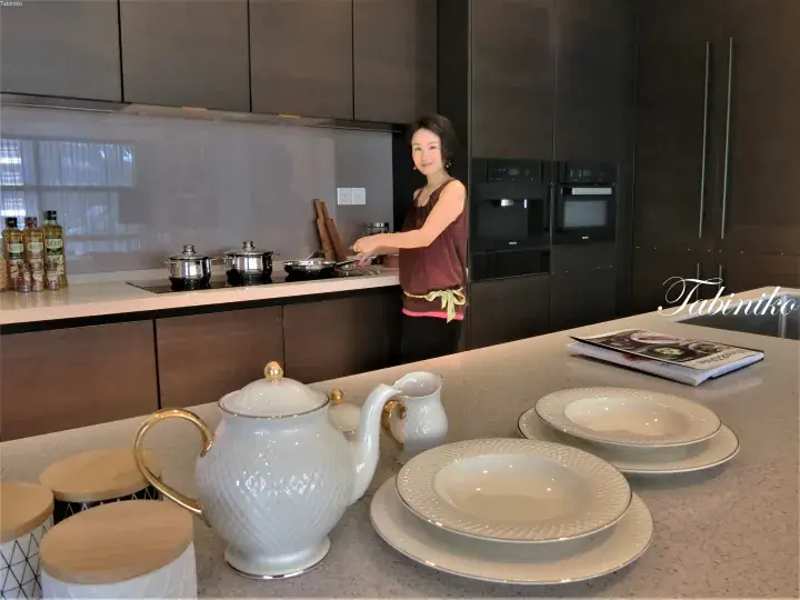 现代厨房中正在烹饪的女性，配有深色橱柜、白色茶具和餐盘。
