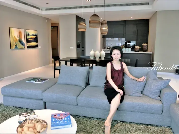 现代豪华公寓客厅中坐在灰色组合沙发上的女性，背景可见厨房和用餐区。
