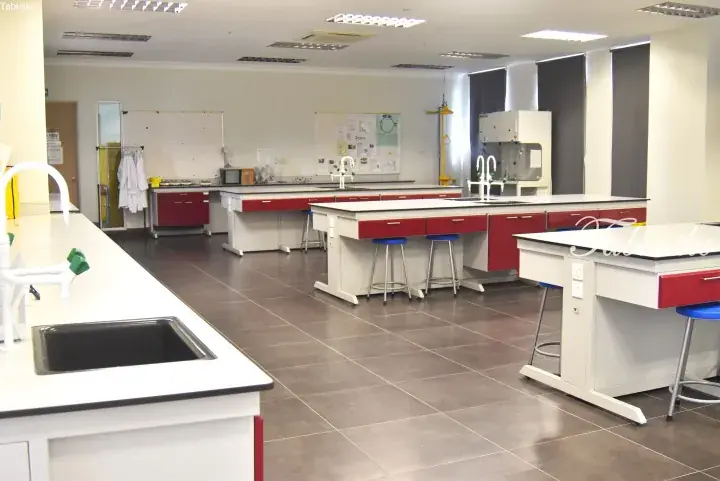 Modern science laboratory with white workbenches, red cabinets, and grey tiled flooring in a Malaysian educational facility.