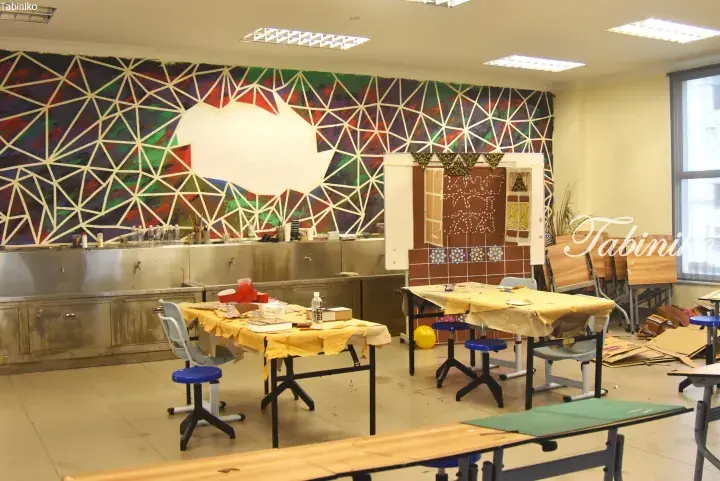 Art classroom with colorful geometric mural, student tables, and craft supplies.
