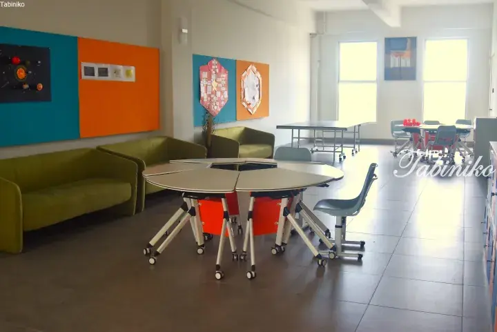 Modern classroom with green sofas, modular tables, and colorful bulletin boards.