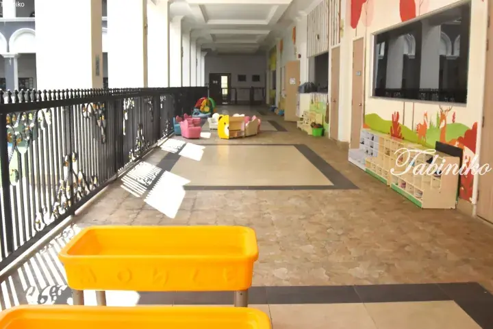 Bright kindergarten corridor with colorful child-sized furniture, shoe lockers, and a yellow activity table.