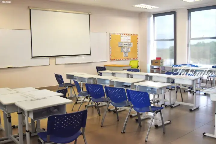 Bright classroom with white desks, blue chairs, projector screen, and large windows in a modern Malaysian school.