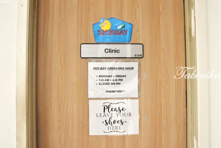 Wooden door of a clinic with a sickbay sign, operating hours, and a notice to leave shoes.
