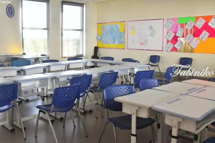Bright classroom with blue chairs and white desks, featuring a world map and student work displays on the wall.