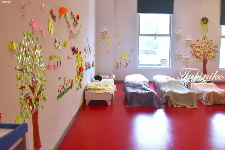 Colorful children’s nap room with red flooring, decorated walls, and small beds.