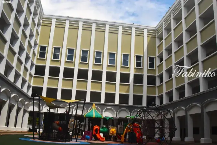 Colorful playground equipment in the courtyard of a modern yellow and white school building.