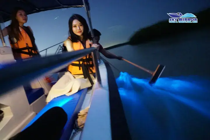 Tourists in life jackets on a boat at night during a Sky Mirror tour in Malaysia, with blue lights illuminating the water.