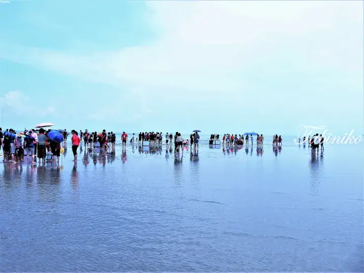 Tourists walking on the reflective sand of the Sky Mirror at Cherating, Malaysia.