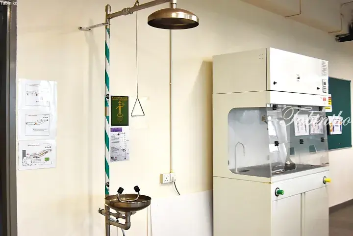 Emergency shower and eyewash station next to a laboratory fume hood in a Malaysian facility.