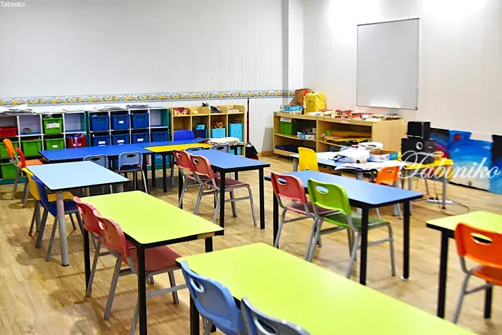 Colorful classroom with blue and green tables, chairs, and storage shelves in a bright learning space.