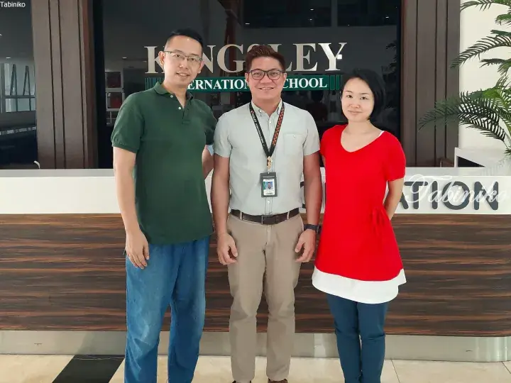Three people standing in front of Kingsley International School reception desk.