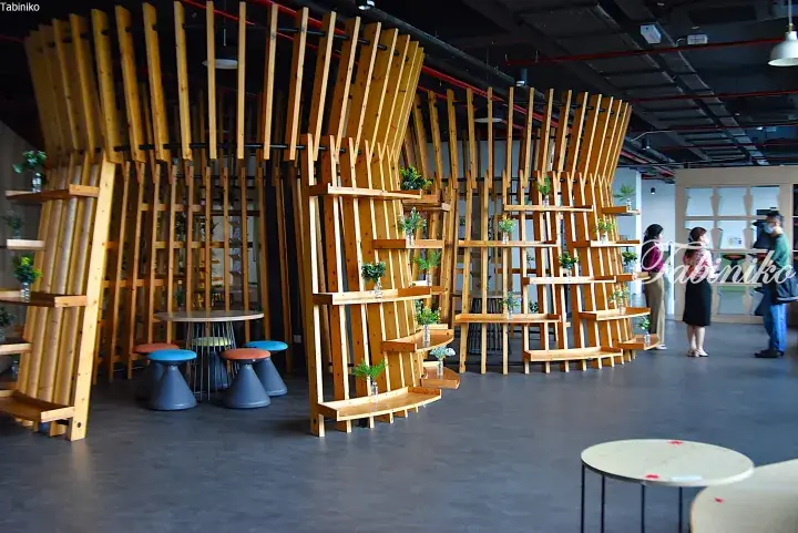 Modern wooden partition with shelves and plants in a bright open-plan office space.