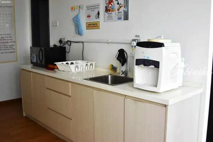 Modern kitchenette with wooden cabinets, sink, microwave, and water dispenser in a Malaysia rental property.