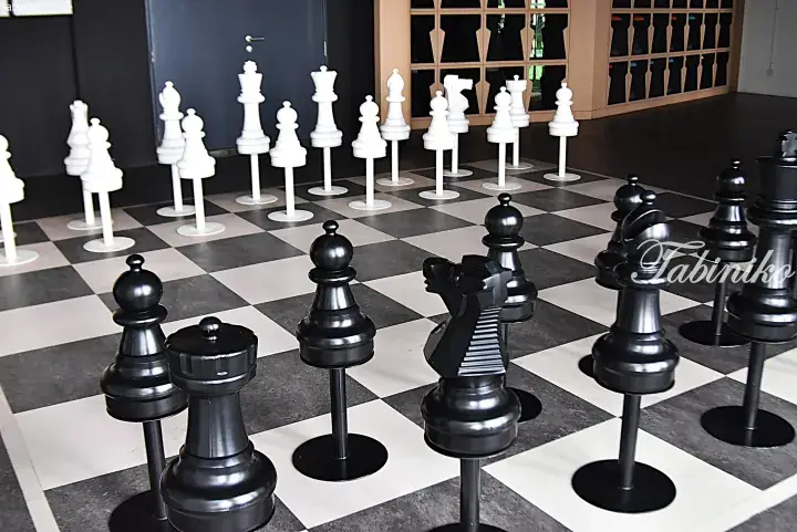 Giant indoor chessboard with oversized black and white pieces on a checkered floor.