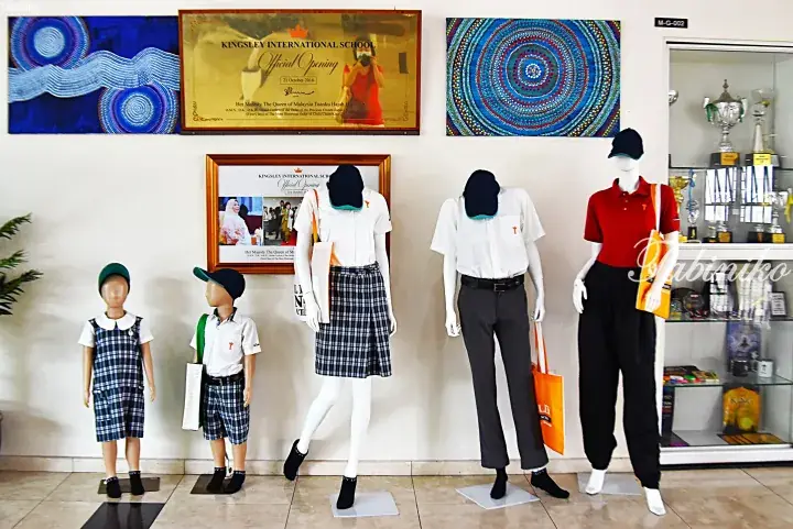 Mannequins display Kingsley International School uniforms in a lobby with official opening plaques and artwork.