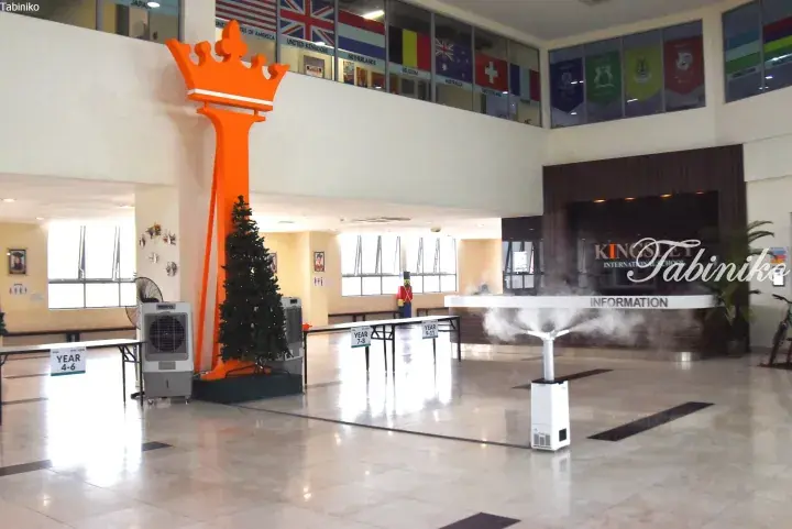 Kingsley International School lobby with a large orange crown sculpture, international flags, and misting fans for cooling.