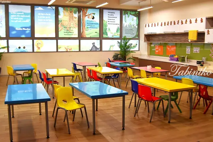 Colorful children’s tables and chairs in a bright classroom with Sesame Street window decals.