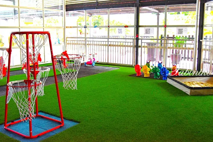 Indoor children’s play area with green artificial turf, red basketball hoops, and colorful spring riders.