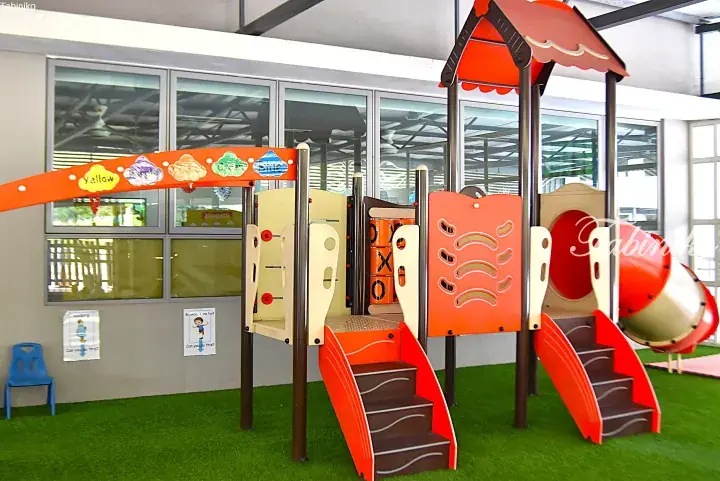Colorful indoor playground with slides, climbing wall, and tic-tac-toe game in a Malaysian school.
