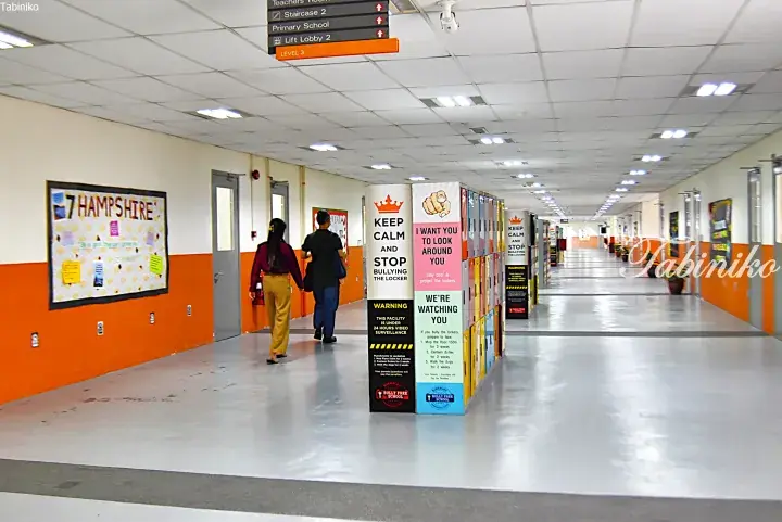 Students walking past lockers with anti-bullying posters in a school hallway.