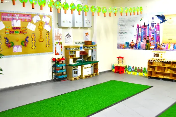 Colorful playroom with toy kitchen, learning posters, and green carpet in a Malaysian early childhood center.