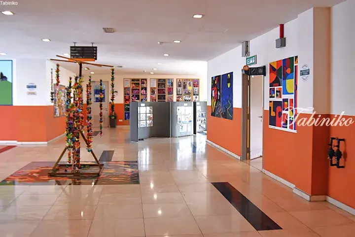 Bright school corridor with orange walls, student artwork displays, and colorful paper craft decorations.
