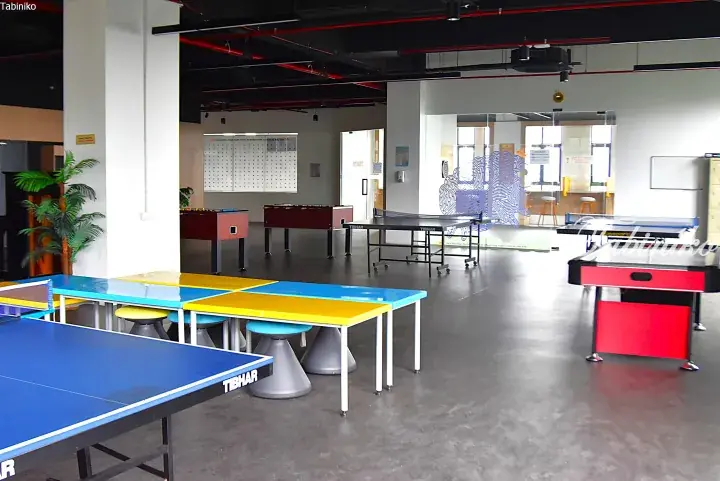 Spacious recreational room with colorful tables, ping pong tables, and foosball tables in a modern facility.