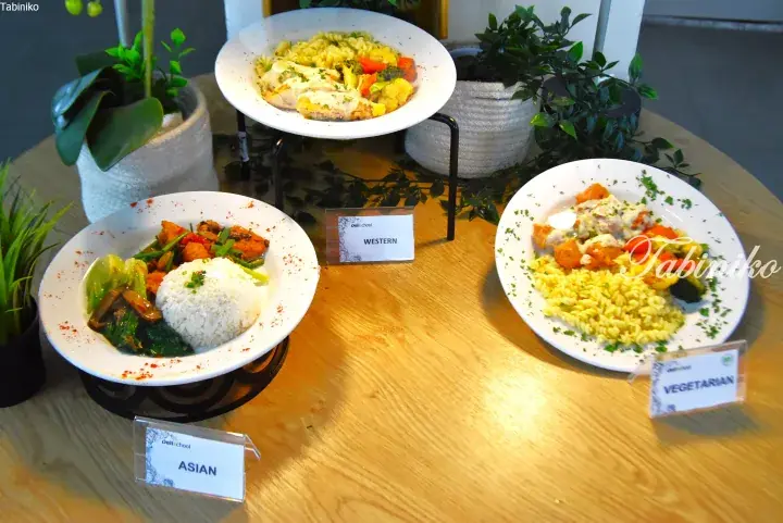 Three plated meals labeled Asian, Western, and Vegetarian displayed on a wooden table with decorative plants.
