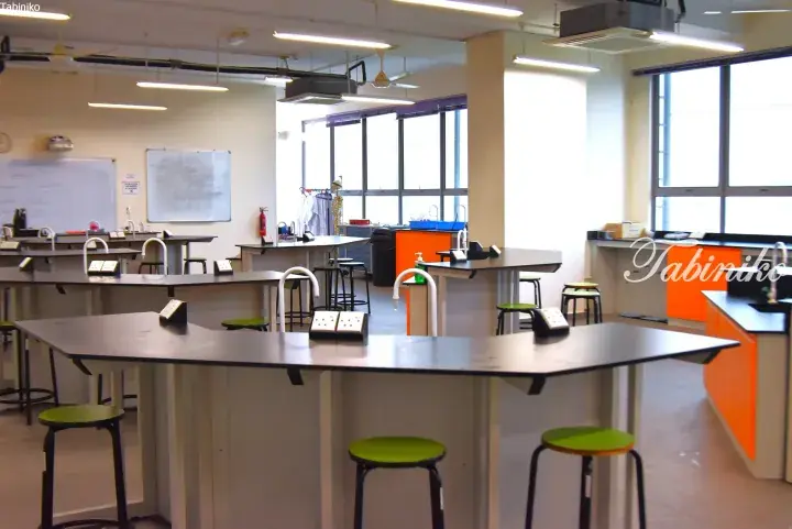 Modern science laboratory with black workbenches, green stools, and bright orange cabinets in a well-lit room.