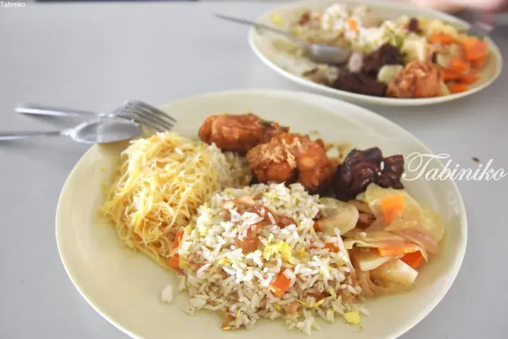 A plate of Malaysian food featuring yellow noodles, fried rice, fried chicken, and vegetables.