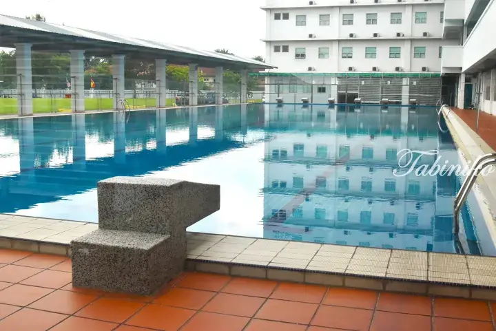 Swimming pool with starting blocks and a white building at a residential complex in Malaysia.