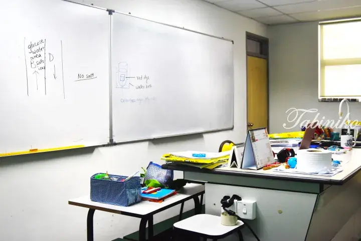 Science classroom with whiteboard diagrams of diffusion experiments and a teacher’s desk with supplies.