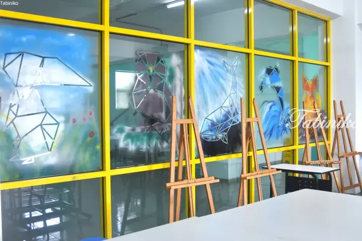 Colorful geometric animal murals on glass windows with yellow frames in an art studio with wooden easels.