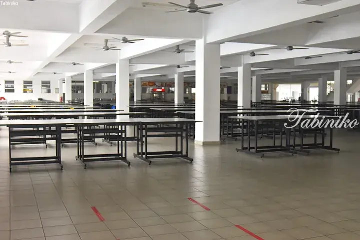 Spacious, empty university cafeteria with rows of tables, white pillars, and ceiling fans.