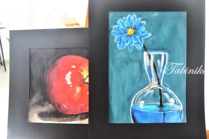 Two framed paintings: a red apple on the left and a blue flower in a glass vase on the right.