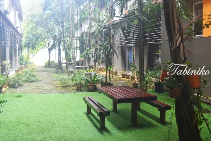 Wooden picnic table on green lawn in a tropical resort courtyard surrounded by palm trees and modern buildings