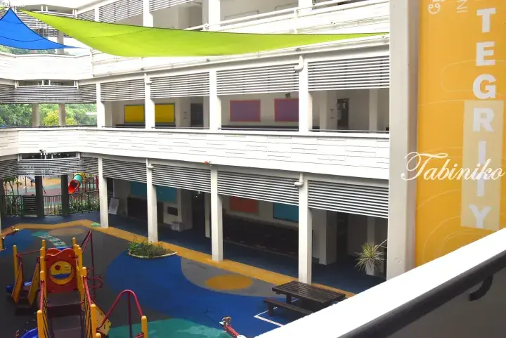 Colorful playground with shade sails and play equipment in the open-air courtyard of a modern Malaysian school building.