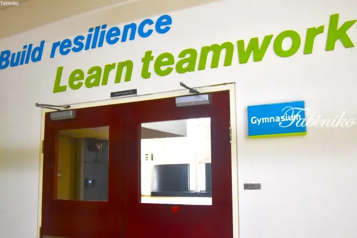 Gymnasium entrance with motivational wall text reading Build resilience Learn teamwork and a blue Gymnasium sign.