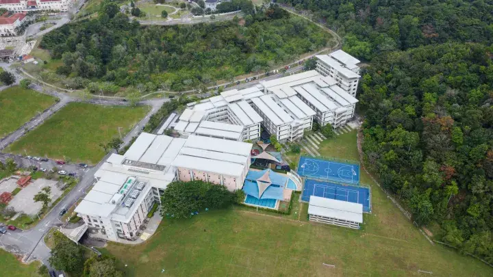 Aerial view of a modern campus with sports courts and pool surrounded by lush greenery in Malaysia.