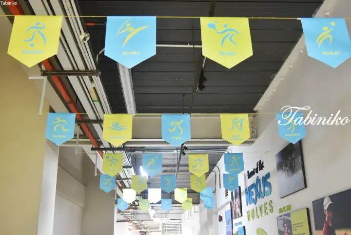 Colorful sports-themed pennants hang from the ceiling in a hallway, with a wall sign reading ‘Home of the NEXUS WOLVES’ visible.