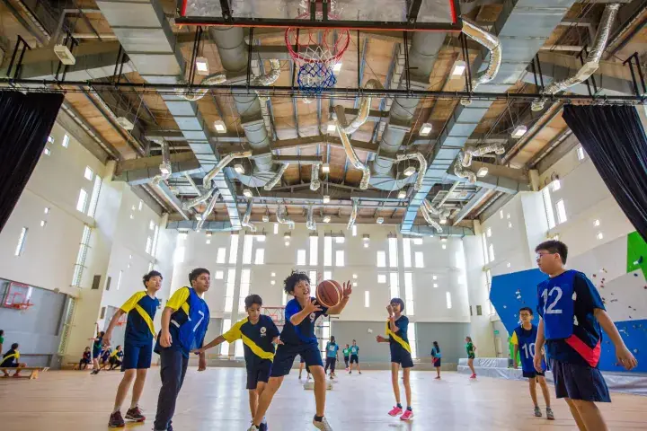 Young boys playing basketball in a bright indoor gymnasium with high ceilings and exposed ductwork.