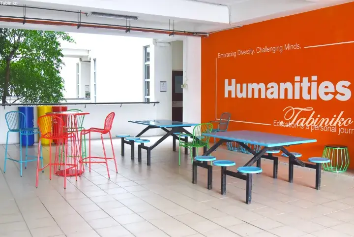 Colorful seating area in a campus Humanities building with orange wall and slogan ‘Embracing Diversity. Challenging Minds.’